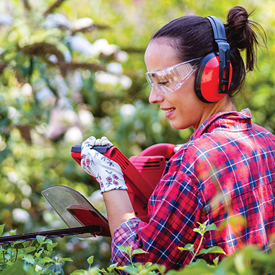 Woman in plaid shirt, safety glasses, and headphones using a power saw